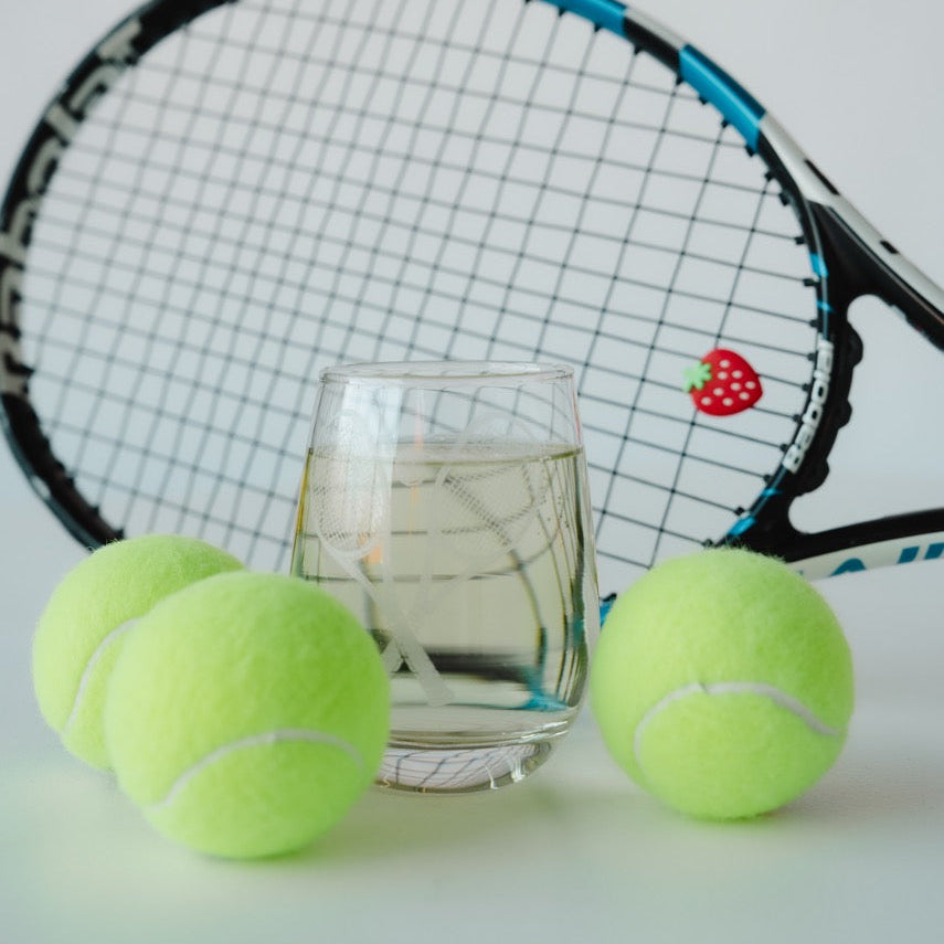 Tennis racket and balls with a glass of water on a light background