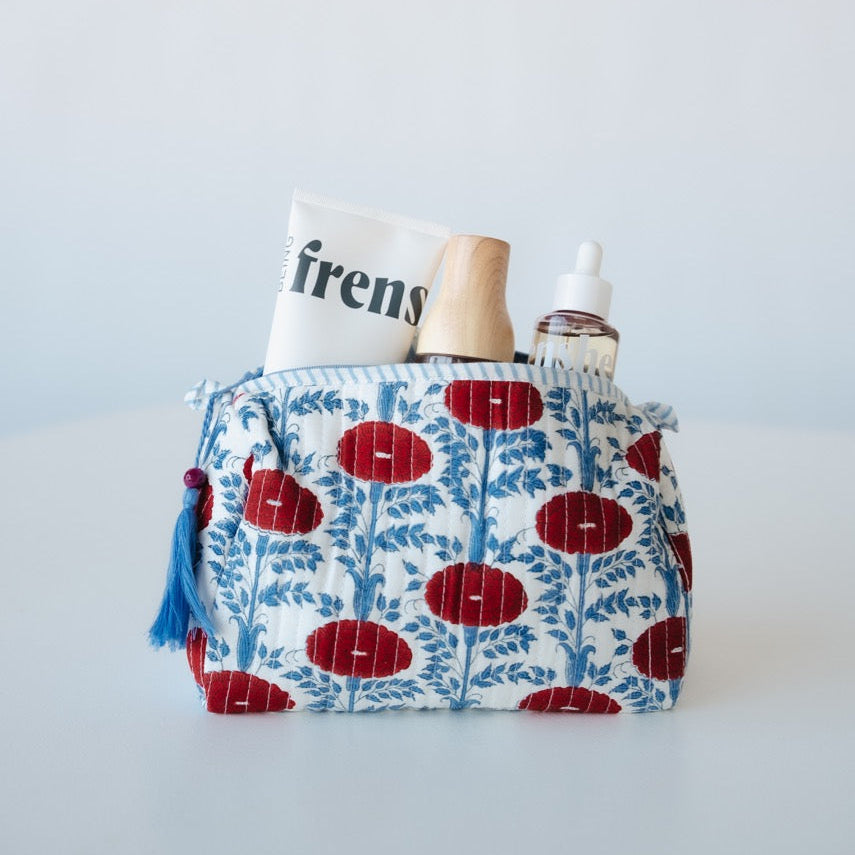 Fabric pouch with floral pattern containing a bottle, tube, and book on a white background