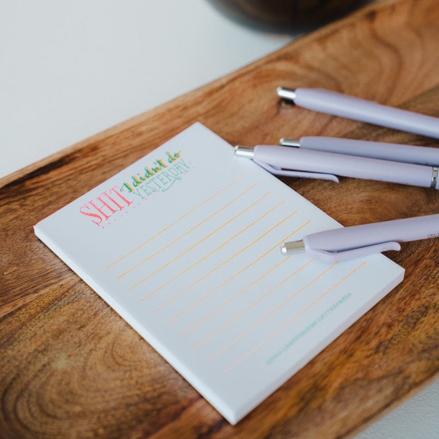Notepad with pen on a wooden surface next to a brown bottle