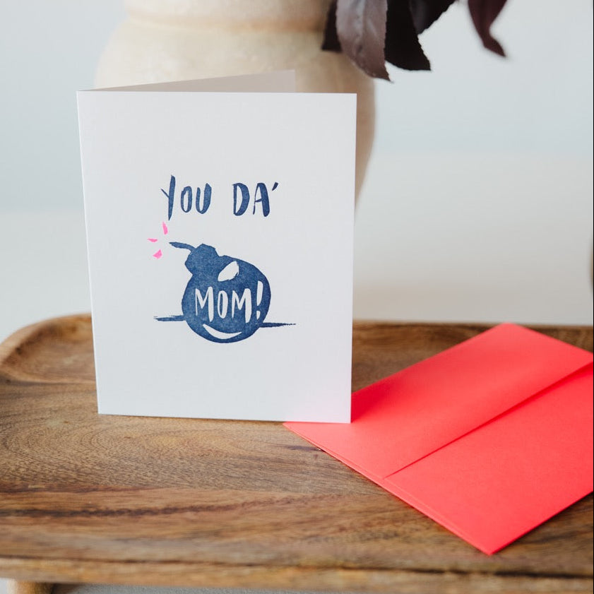 Greeting card with 'You da' Mom!' and envelope on a wooden surface