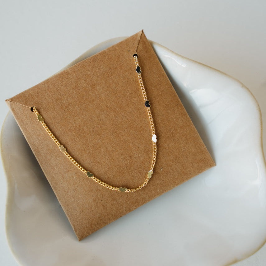 Gold necklace with black beads on a brown jewelry card on a white surface