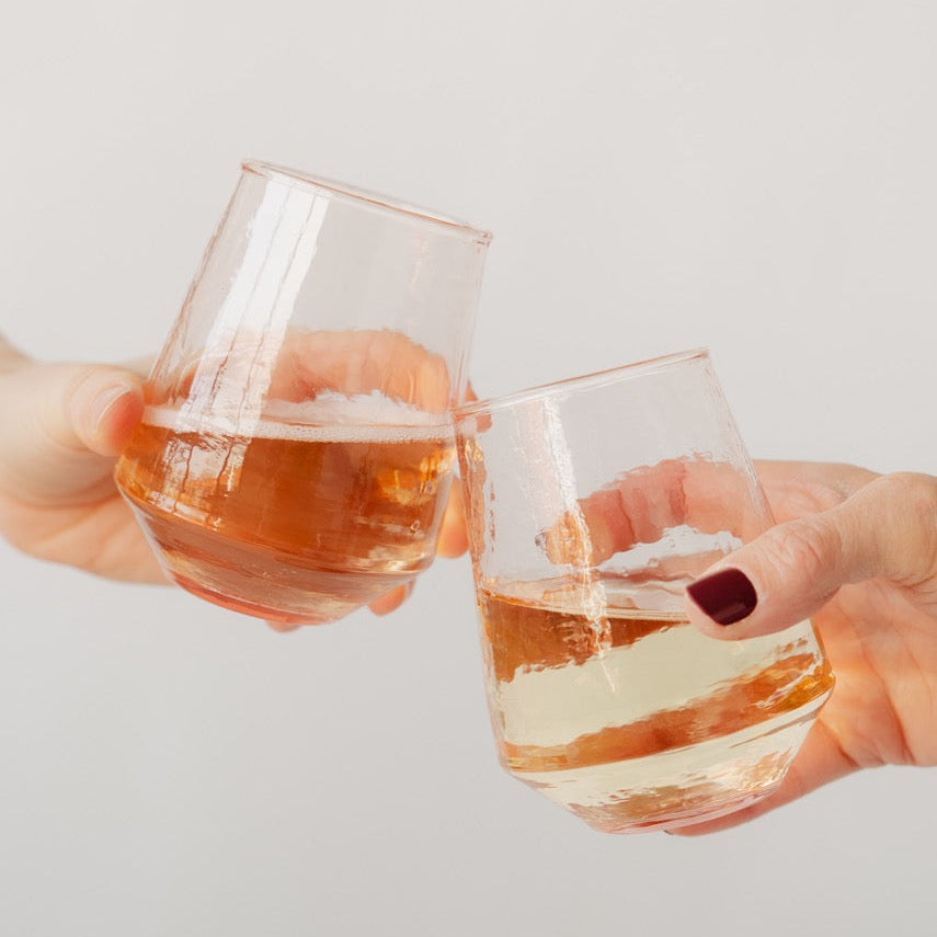 Two hands holding glasses of orange liquid against a light gray background